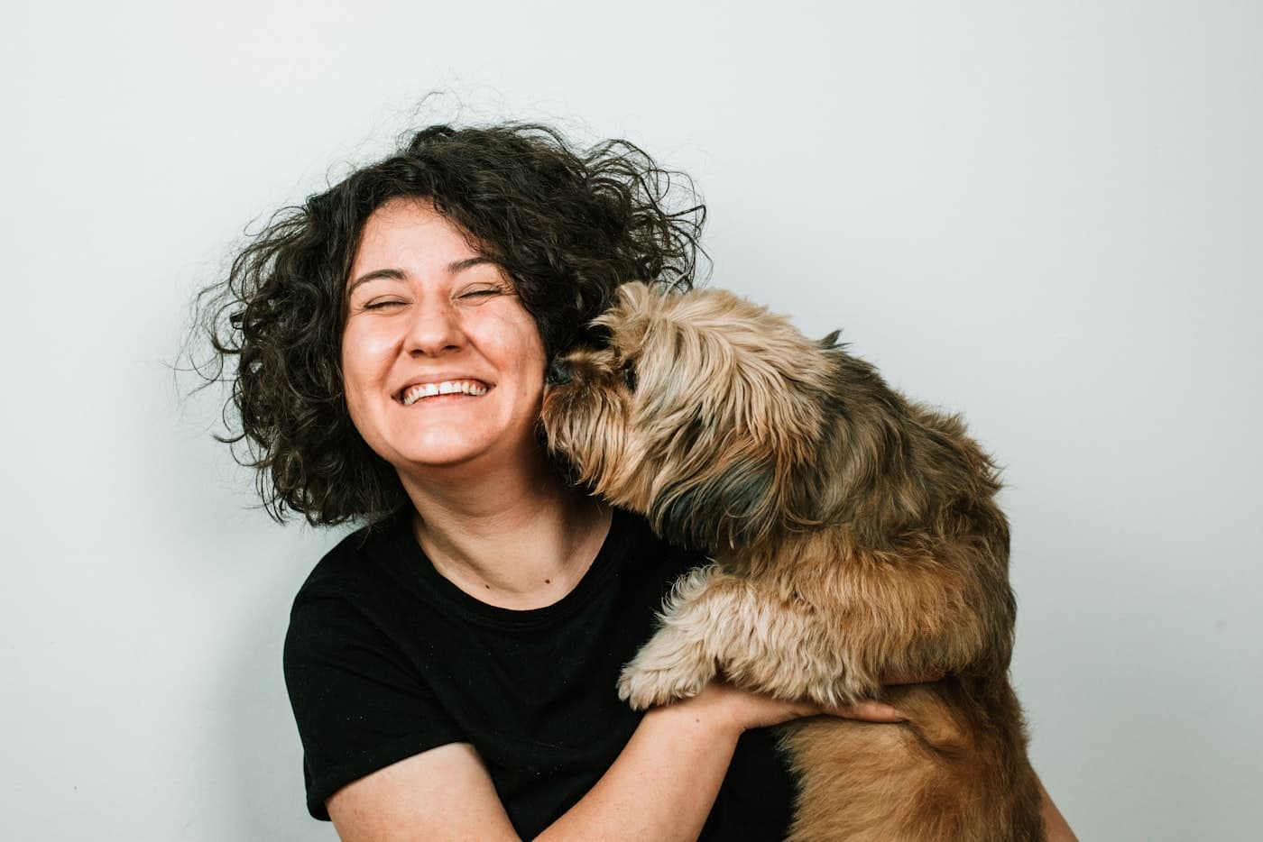 Pet owner laughing as her small dog licks her cheek