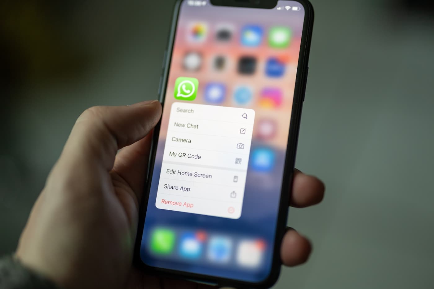 Hand holding an iPhone with the WhatsApp app icon and its quick-action menu open